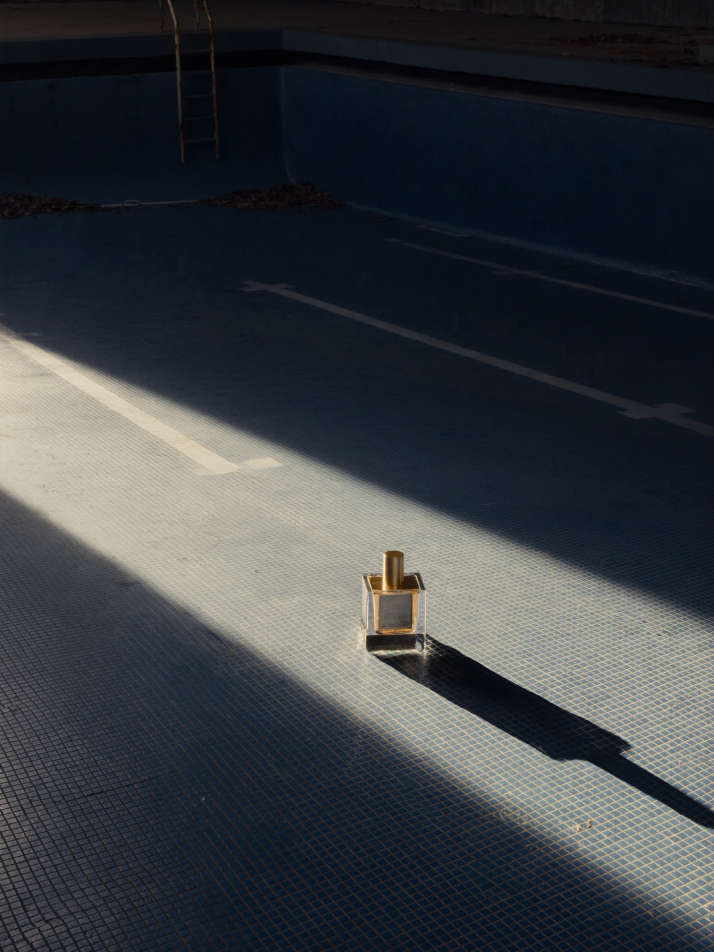 Flacon de parfum doré dans une piscine vide au soleil — image produit